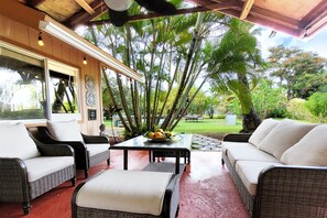 A covered outdoor seating area with wicker furniture and a table with fruit.