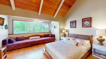 A bedroom with a large bed, a sofa bed, wooden flooring, a ceiling fan, and a window with blinds.