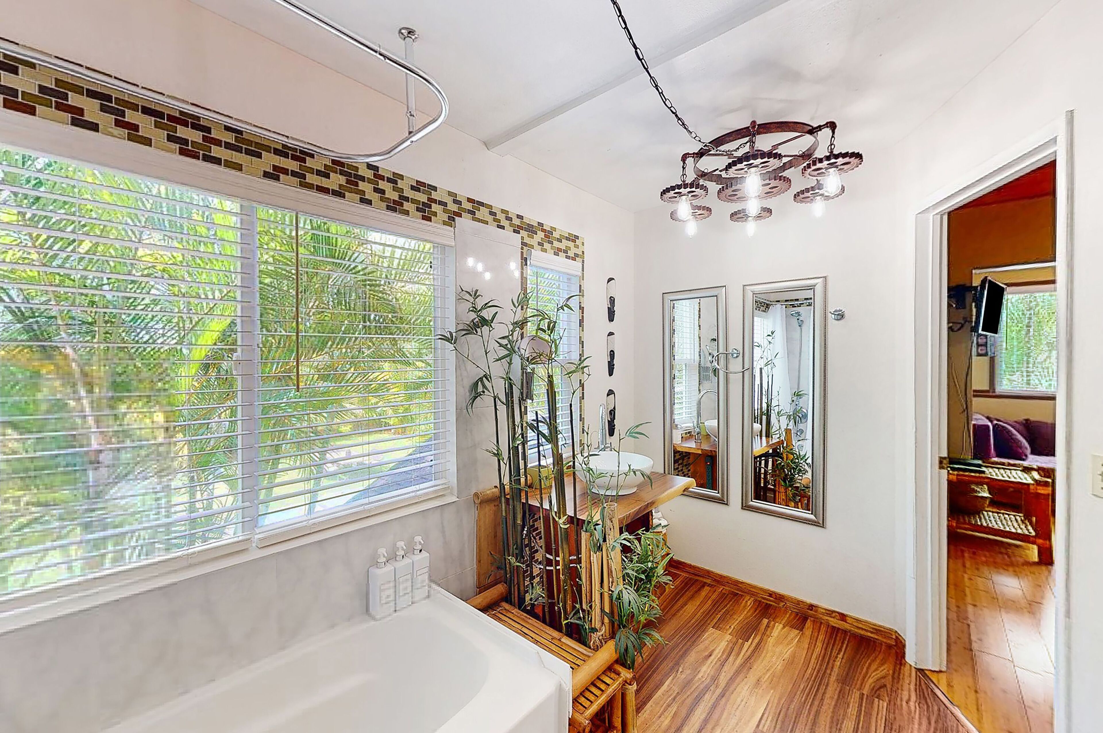 A bathroom with a bathtub, a sink, and a mirror. There are bamboo plants and a wooden shelf.