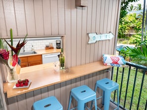 A kitchen with wooden countertops, a sink, and a coffee maker. There are two blue stools and a sign on the wall that says "GONE TO BE".