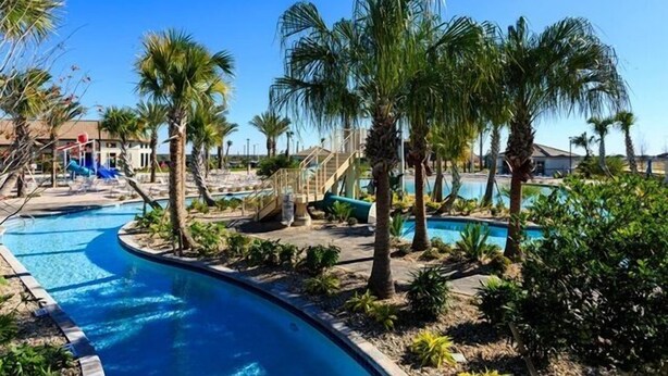 A swimming pool area with palm trees, a slide, and a building in the background.