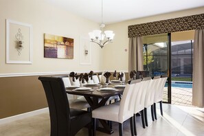 A dining area with a dark wooden table set for six, white chairs, and a chandelier. - 8BR ULTIMATE LUXURY, PRIVATE POOL & SPA, HOME THEATRE. CLOSE TO DISNEY, GOLF (Davenport)