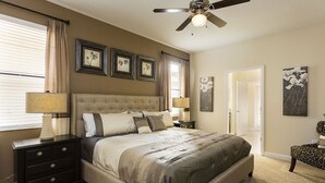 A bedroom with a large bed, two bedside tables, a ceiling fan, and framed pictures on the wall.