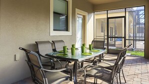 A patio with a glass table and chairs, a window, and a door leading to an outdoor area.