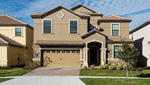 A two-story residential house with a beige facade, a garage, and a landscaped front yard.