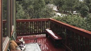 Una terraza de madera con un banco y una mesa, con vistas a un valle boscoso con un río.