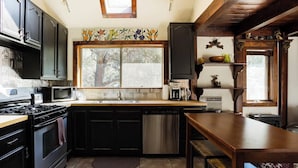 Una cocina con armarios negros, lavavajillas de acero inoxidable y una mesa de madera.