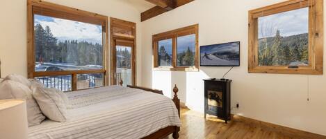 A bedroom with a bed, wooden beams, large windows with scenic views, and a fireplace.