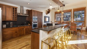 A kitchen with wooden cabinets, stainless steel appliances, a bar area with stools, and large windows offering a view of a snowy landscape. - Retreat at Union Creek II:  Easy Walk to Lift, Hot Tub, Foosball, Shuttle (Copper Mountain)