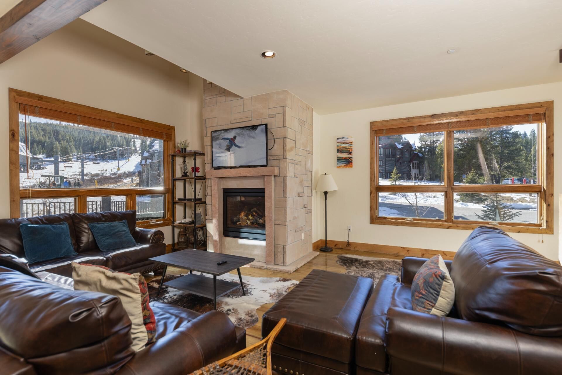A cozy living room with leather sofas, a fireplace, and large windows offering a snowy mountain view.