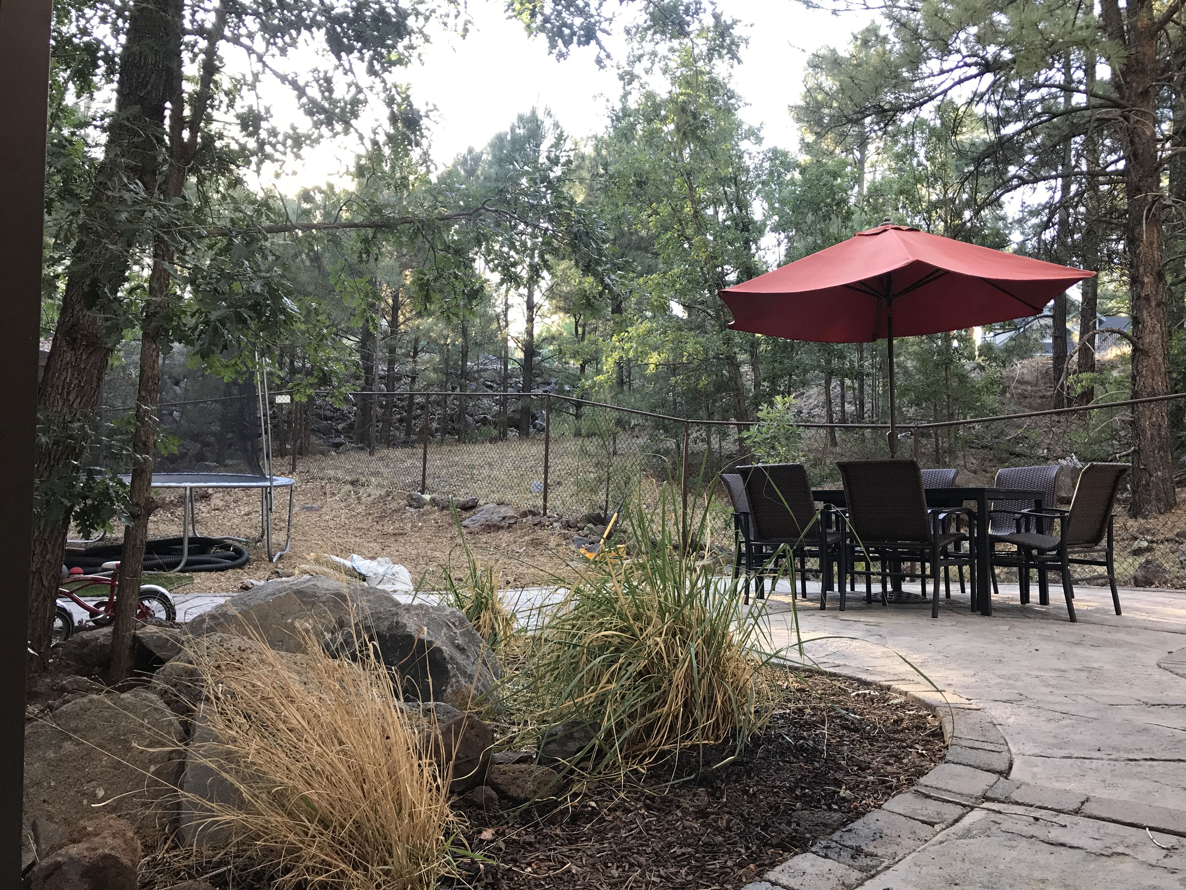An outdoor patio area with a red umbrella, dining table, and chairs.