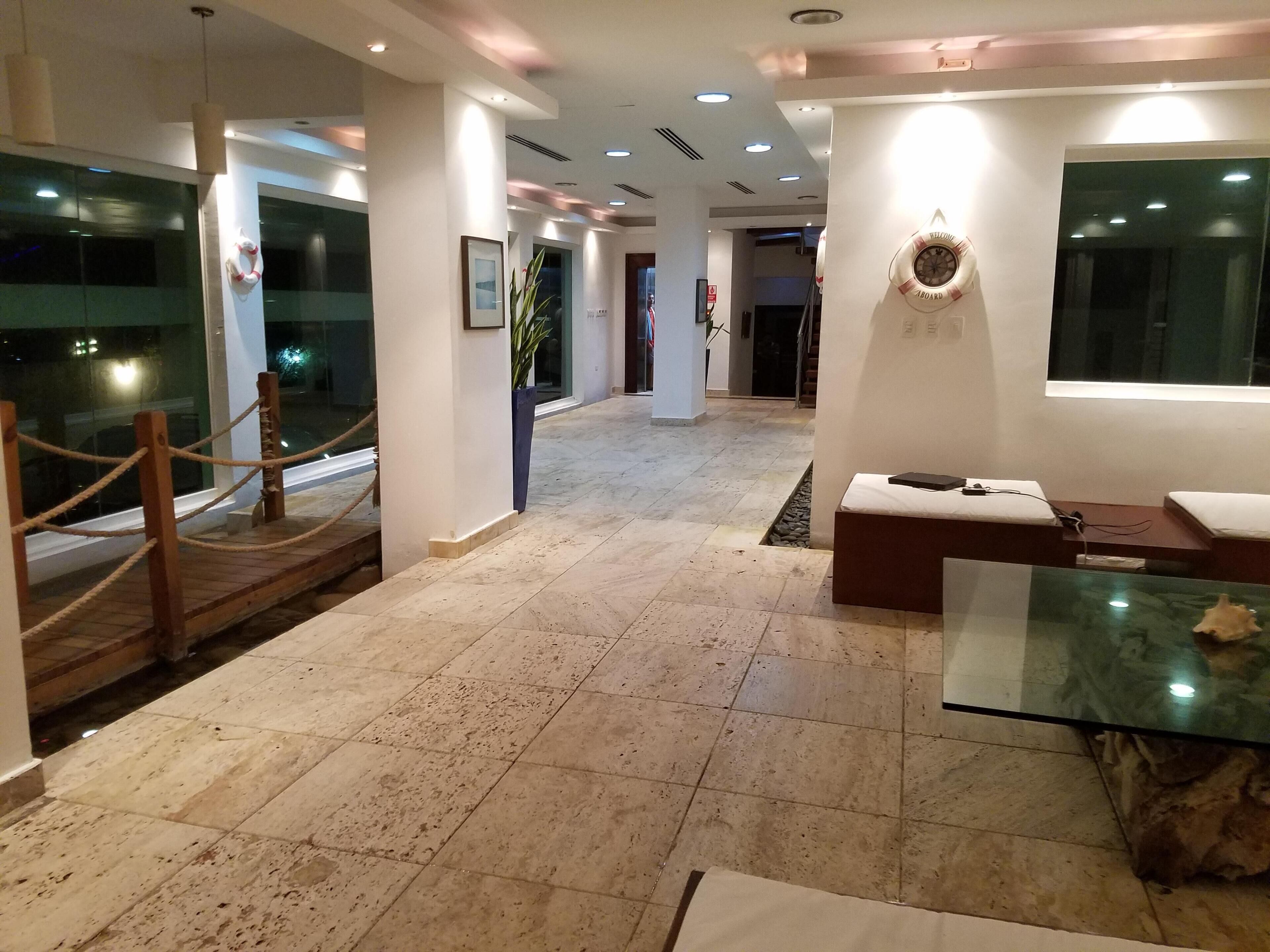 Un hall d’hôtel doté d’un sol en marbre, d’un comptoir de réception, d’un espace salon avec une table en verre et d’un escalier menant à un autre niveau.