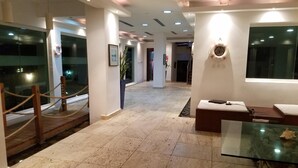 En hotellobby med ett marmorgolv, en receptionsdisk, en sittgrupp med ett glasbord och en trappa som leder till en annan våning.