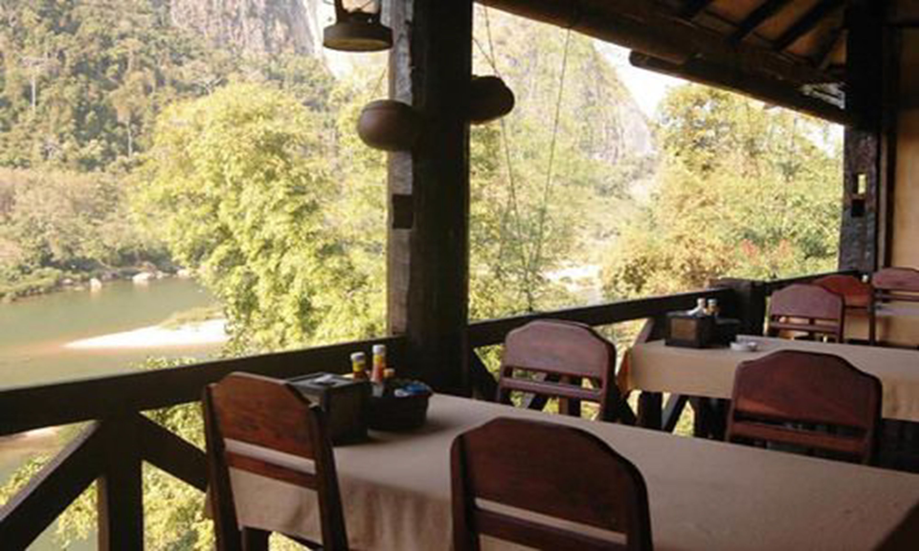 A dining area with tables and chairs overlooking a river and forested landscape.