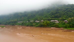 A river with houses along its banks, surrounded by dense greenery and a misty atmosphere. - Nong Kiau Riverside (Nong Khiaw)