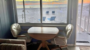 A room with a large window overlooking a beach. There is a table and two chairs in the room.