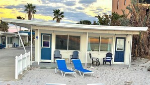 A beachside building with a covered area, two lounge chairs, and a small table.