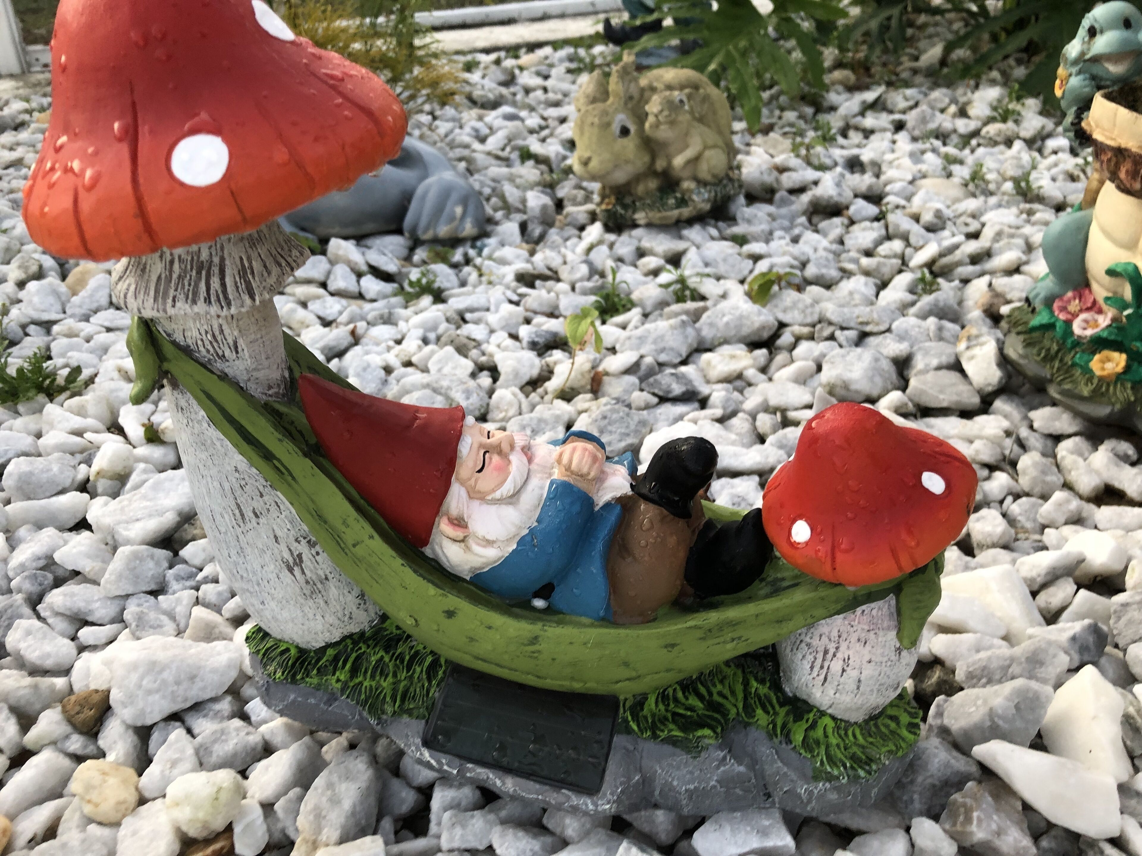 Un jardin agrémenté d’un banc en forme de champignon, d’une sculpture de gnome et d’une statuette de lapin.