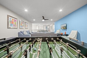 A room with a foosball table, a sofa, and a television mounted on the wall. - No Rear Neighbors • Pool & Spa • Game Room • Lazy River • Gated Resort (Kissimmee)