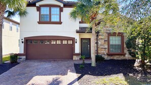 A two-story house with a brown garage door, a stone exterior, and a well-maintained driveway. - MEGA Mansion! Family Memories Made Here! Westside Resort Waterpark (Kissimmee)