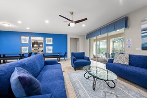 Ein modernes Wohnzimmer mit blauen Sofas, einem Glastisch und einem Deckenventilator.