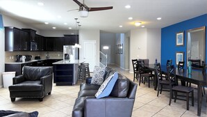 A modern living room with a leather sofa, a dining area with a table and chairs, a kitchen with dark cabinets and appliances, and a ceiling fan. - MEGA Mansion! Family Memories Made Here! Westside Resort Waterpark (Kissimmee)