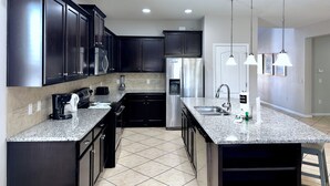 A modern kitchen with dark cabinets, stainless steel appliances, granite countertops, and pendant lighting. - MEGA Mansion! Family Memories Made Here! Westside Resort Waterpark (Kissimmee)