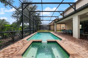 Una piscina con un recinto in vetro, circondata da un patio in mattoni e una recinzione.