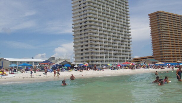 Un hotel frente a la playa con varios balcones, una playa de arena y cielos azules despejados.