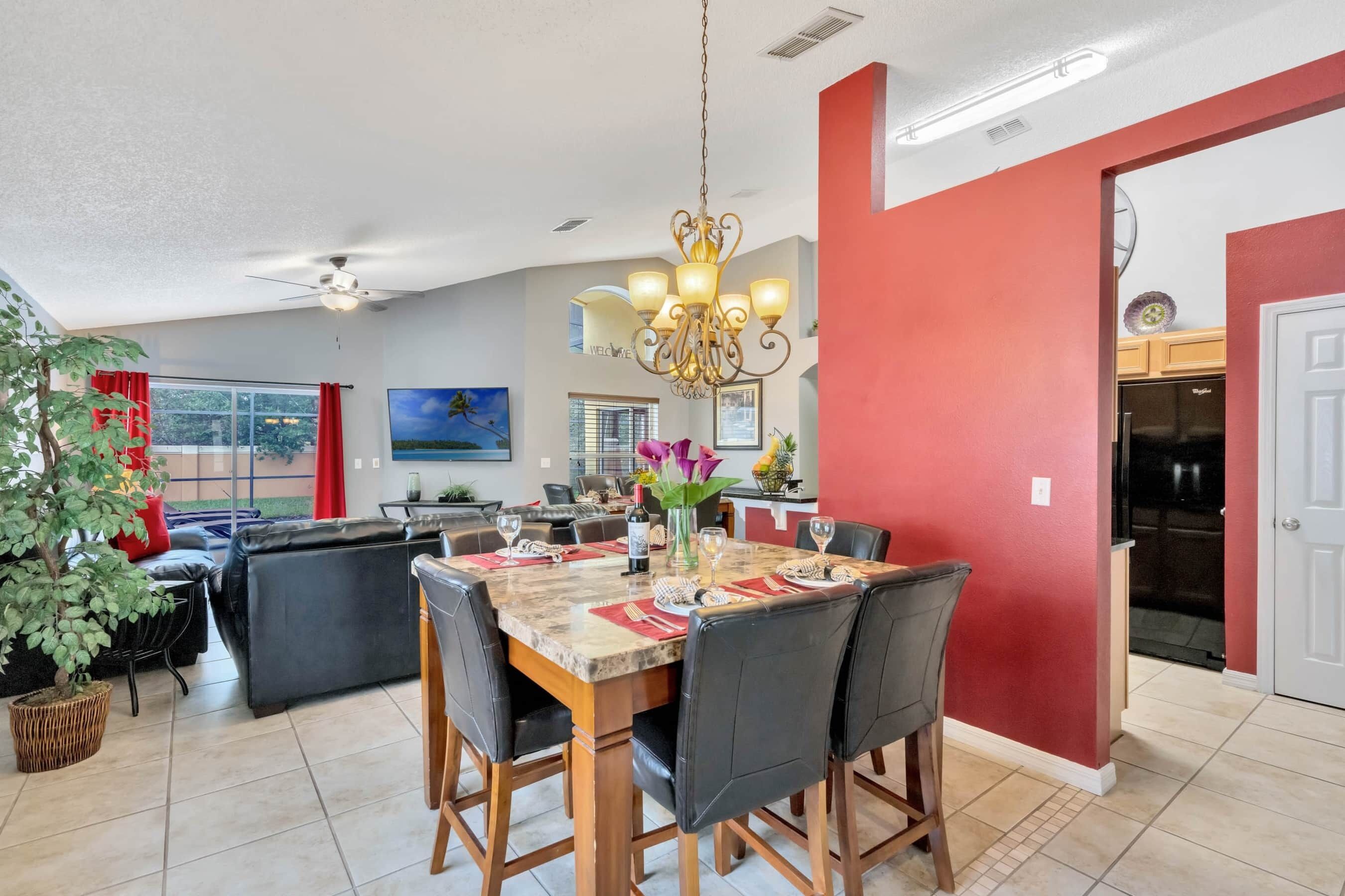 Un vaste espace de vie comprenant une salle à manger avec une table pour six personnes, une grande fenêtre et un mur d’accent de couleur rouge.