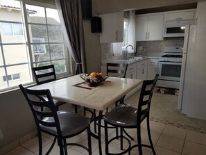 A kitchen with white cabinets, a stove, and a microwave. There is a dining table with chairs and a fruit bowl on it.