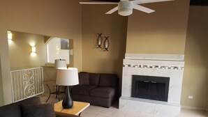 Un salon avec une cheminée, un canapé, une lampe et un ventilateur de plafond.