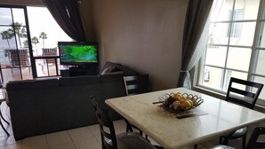 Un salon comprenant un canapé, un téléviseur, une table à manger avec des chaises et une fenêtre avec des rideaux.