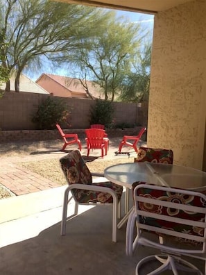 A patio area with a round table and chairs, red plastic chairs, and a view of a house and trees.