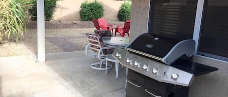 Un espace barbecue extérieur doté d’un meuble intégré, d’une table avec des chaises et d’un coin salon sur la terrasse.