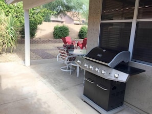 An outdoor grill area with a built-in cabinet, a table with chairs, and a patio setting.