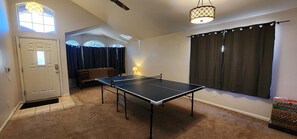 A room with a ping pong table, a door, a window with curtains, a lamp, and a ceiling fan. - Quiet desert getaway, ping-pong, BBQ, citrus (Phoenix)