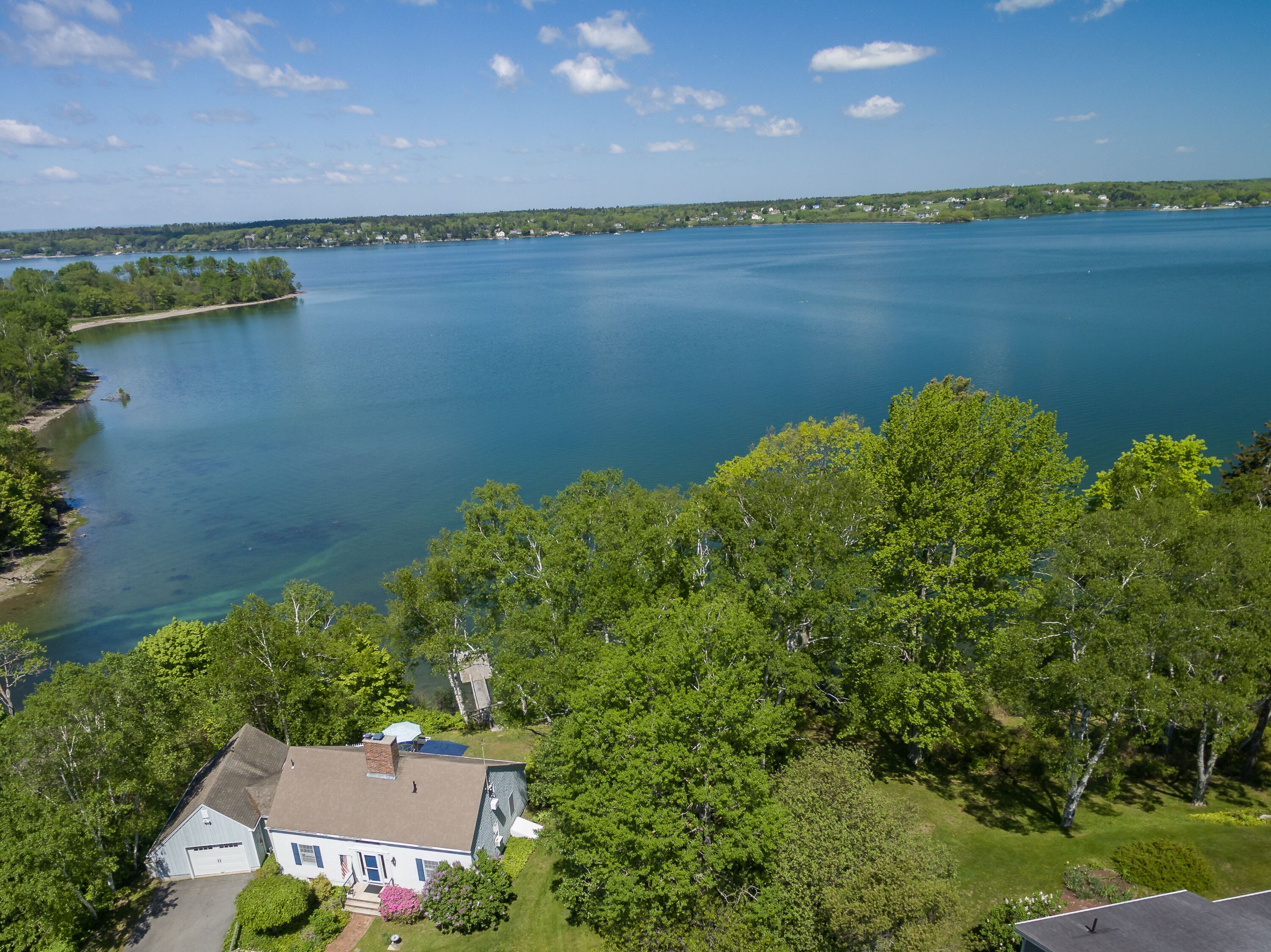 A house with a garage, surrounded by dense trees and a large body of water.