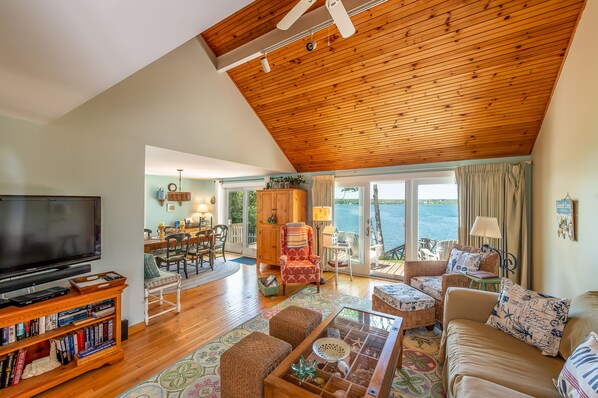 A spacious living area with a wooden ceiling, a television, a bookshelf, and a view of the outdoors.