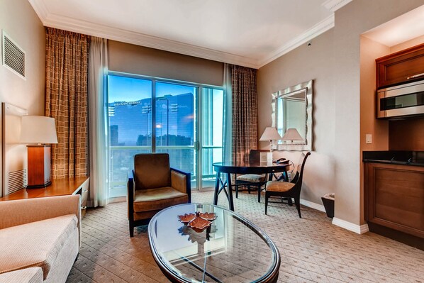 A hotel room with a large window, a glass coffee table, a sofa, a dining table with chairs, and a kitchen area. - MGM Signature Jr.Penthouse StripView, Balcony, Pool, No resort fee, FREE parking (Las Vegas)