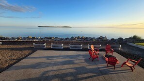 Un espace extérieur aménagé avec des chaises rouges et des jardinières, offrant une vue sur une étendue d’eau paisible et sur la terre ferme au loin.