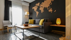 Una sala de estar moderna con un mural de un mapa mundial, un sofá gris con cojines amarillos, una mesa de centro, una lámpara y una mesita de noche de madera.