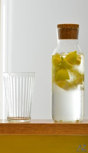 Une bouteille en verre transparent, fermée par un bouchon en liège, et un verre placés à côté sur une surface en bois.
