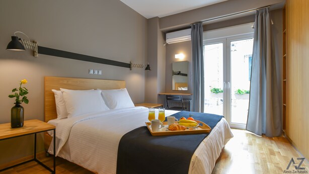 Una habitación de hotel con cama, mesita de noche y bandeja de desayuno con croissants, jugo y café.
