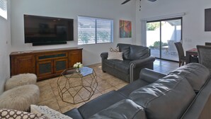 Ein Wohnzimmer mit einem großen Flachbildfernseher, einem Deckenventilator, einer Couch, einem Couchtisch und einer Glastür zum Außenbereich.