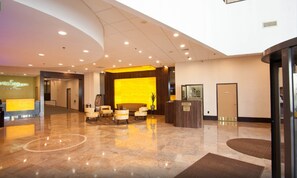 Un hall d’hôtel comprenant un comptoir d’accueil, un espace salon et un poste de sécurité.