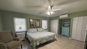 A bedroom with a bed, a chair, a dresser, a closet, and a ceiling fan.