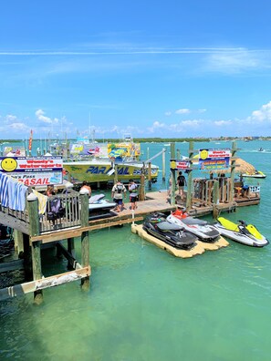 A pier with jet skis docked, wooden walkways, and signs advertising water sports.