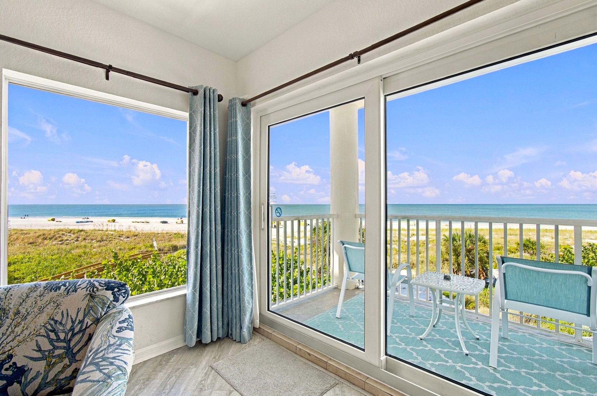 A balcony with a view of the beach, a chair, and a table.