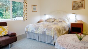 A bedroom with a bed, a chair, a bedside table, a lamp, a picture on the wall, and a window with curtains.